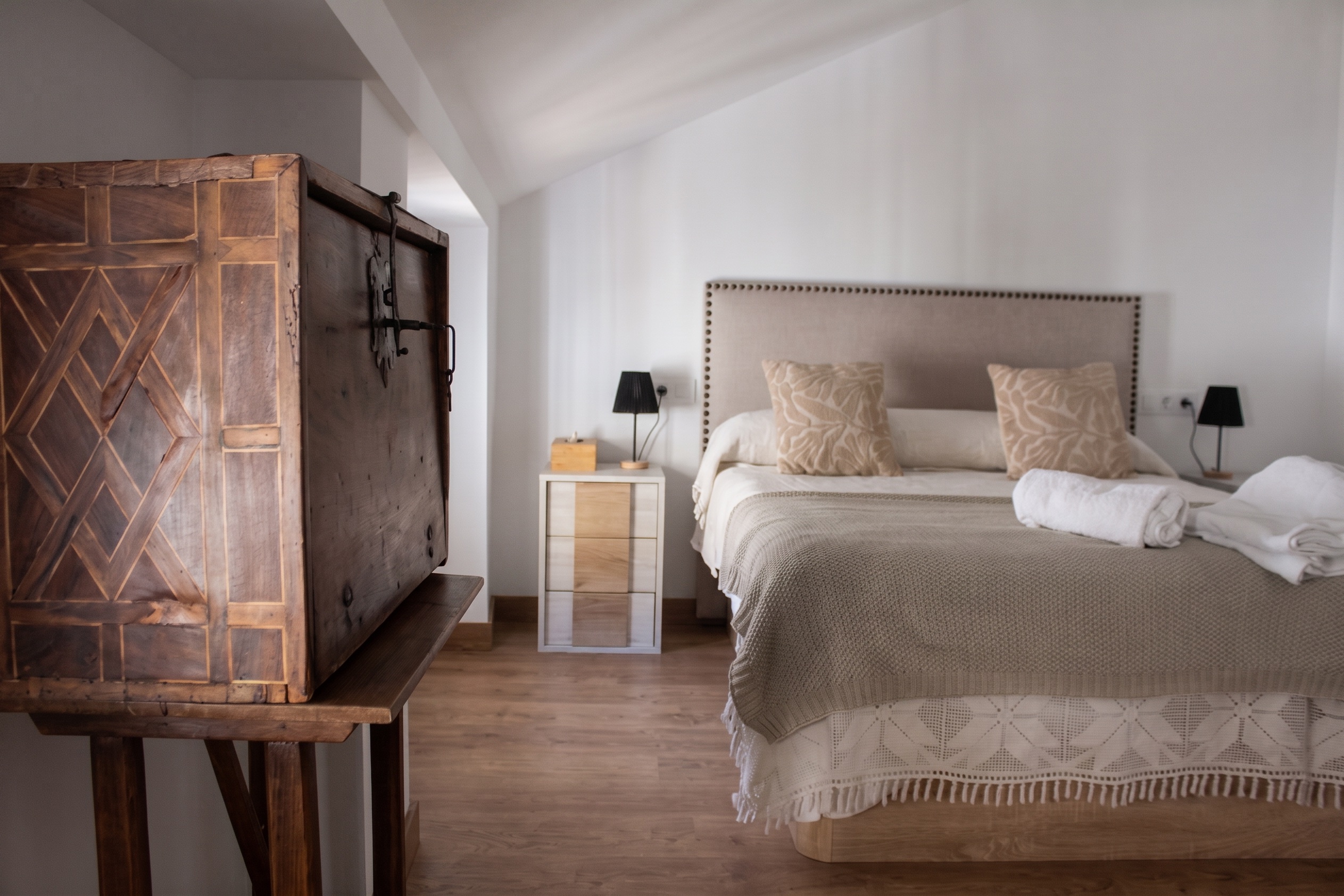 Arcón antiguo de madera en primer término y la cama del Ático detrás