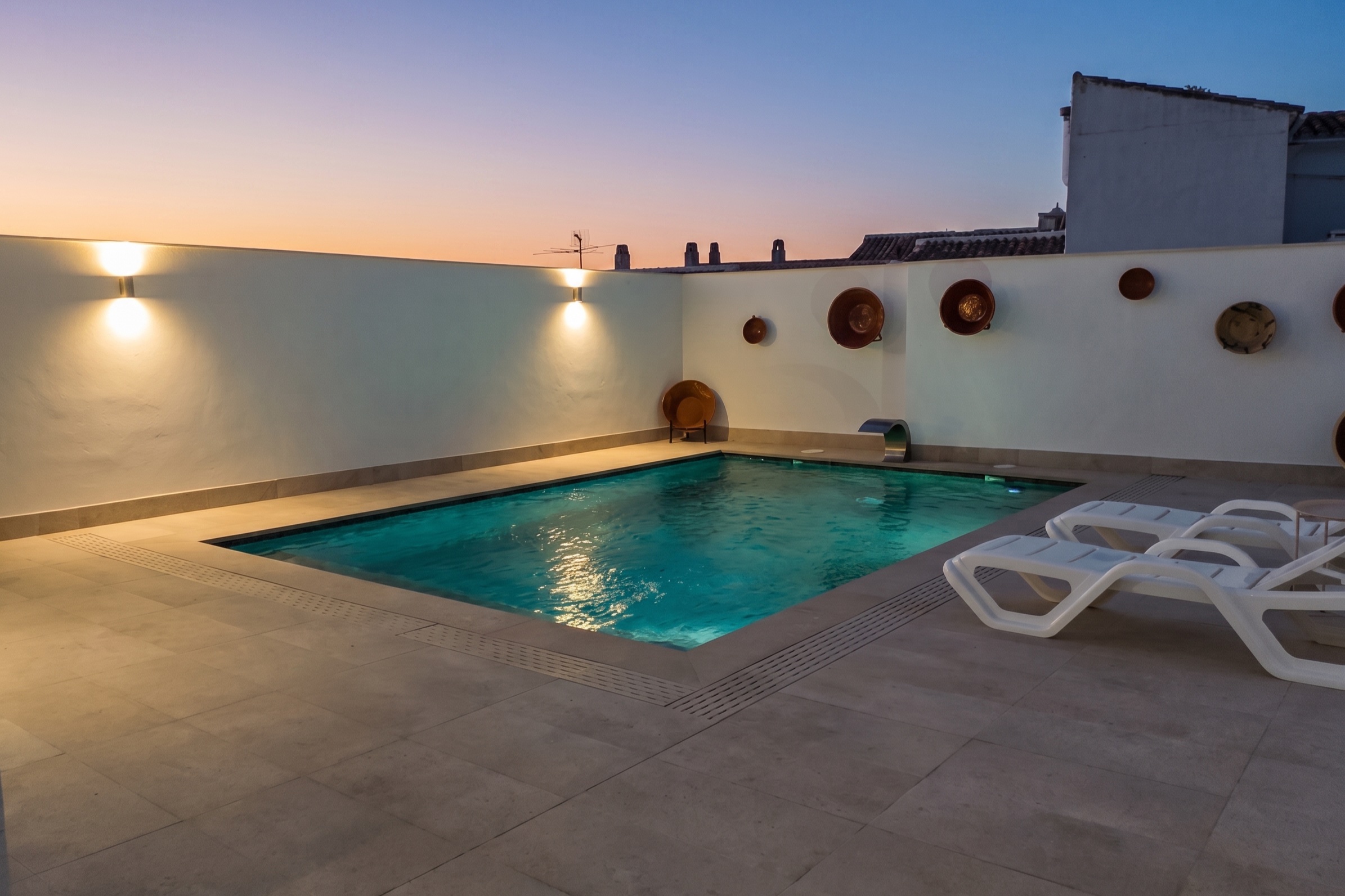 La piscina iluminada en hora azul, con los lebrillos de barro en el muro