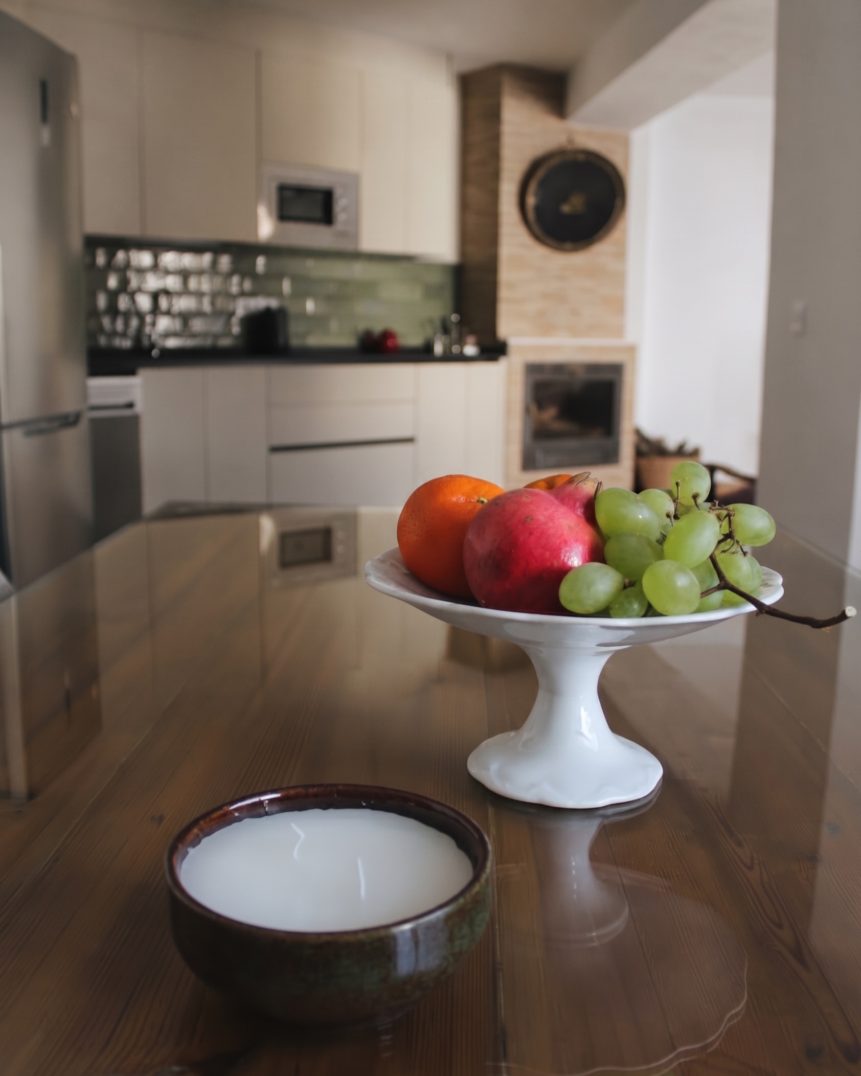 Frutero con granada y uvas sobre la mesa, con la cocina de El Principal al fondo